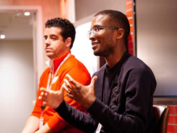 Redwings employee gesticulating and smiling while sitting next to another employee, sitting in a Redwings conference room.